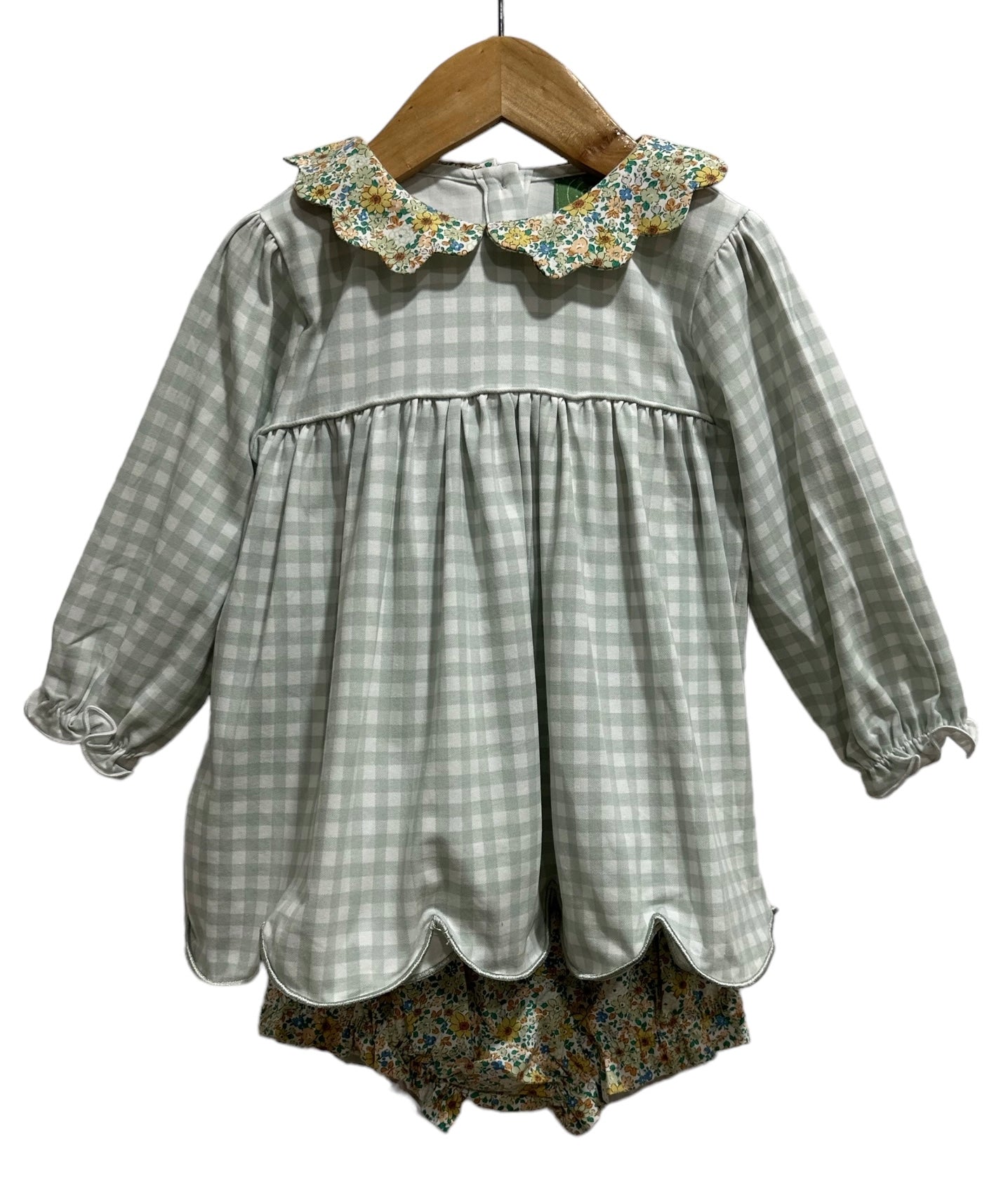 A children's long-sleeve blouse and matching shorts set hanging on a wooden hanger against a plain white background. The top is light sage green and white gingham with a floral-patterned ruffled collar, and the shorts are a matching multicolor floral print.