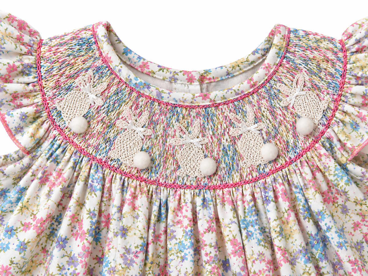 Close-up of hand-smocked Easter bunnies with white bows and pom-pom tails on a pastel floral girls bubble