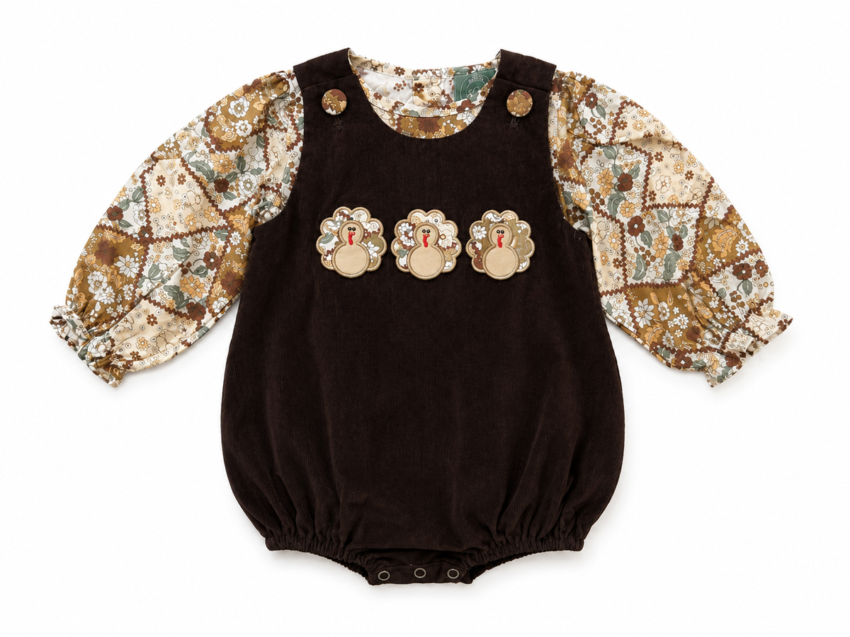 A baby long-sleeve romper with a dark brown corduroy body, patterned sleeves in beige, brown, and green, and three turkey appliqués on the chest.