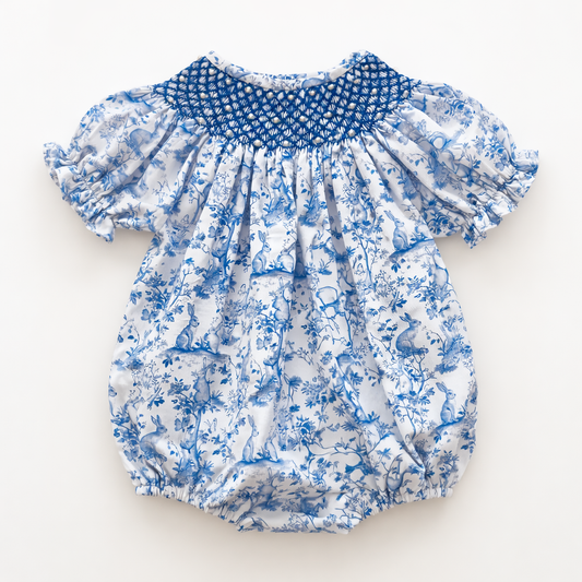Blue and white bunny print baby bubble romper with hand-smocked blue neckline with pearls and ruffled sleeves.