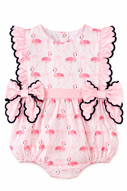 Girls pink flamingo bubble romper with navy scalloped ruffle trim, pink waistband, and statement side bows.