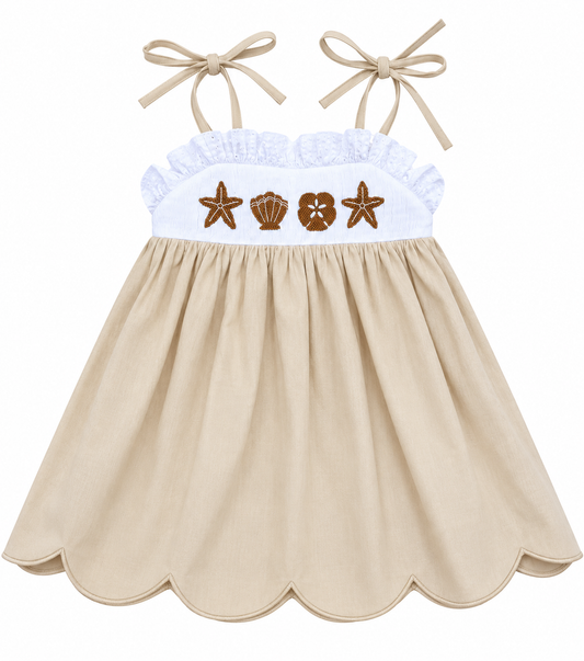 Girls’ beige hand-smocked seashell sundress with embroidered starfish and shells, white ruffle bodice, tie straps, and scalloped hem.