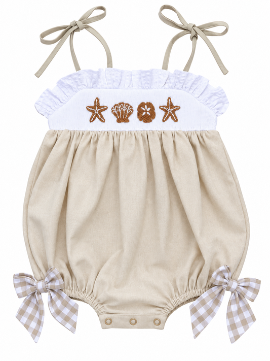 Girls’ beige beach bubble romper with embroidered starfish and seashells, white ruffle trim, tie straps, and gingham bows.
