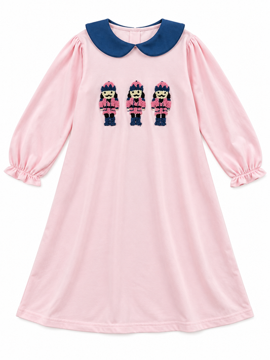 Pink girls’ Christmas dress with navy Peter Pan collar, long sleeves, and three embroidered nutcracker soldiers on the front.