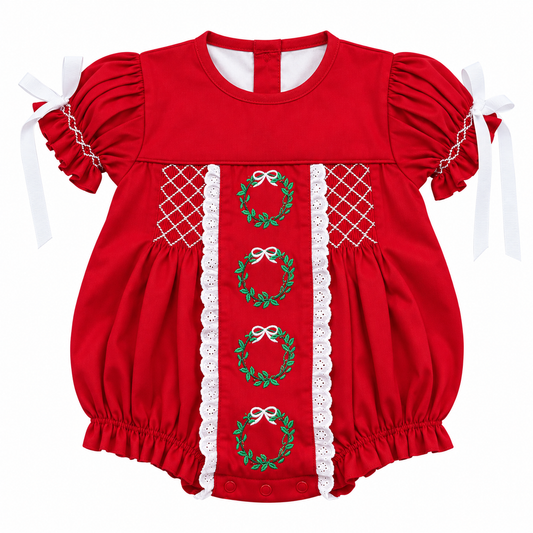 A red baby romper with short puff sleeves, white lace trim, and green embroidered wreaths with white bows down the center front.